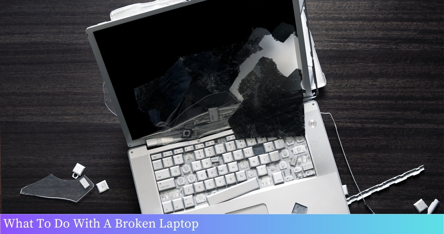 A broken laptop lying on a table, showing a cracked screen and detached keyboard.